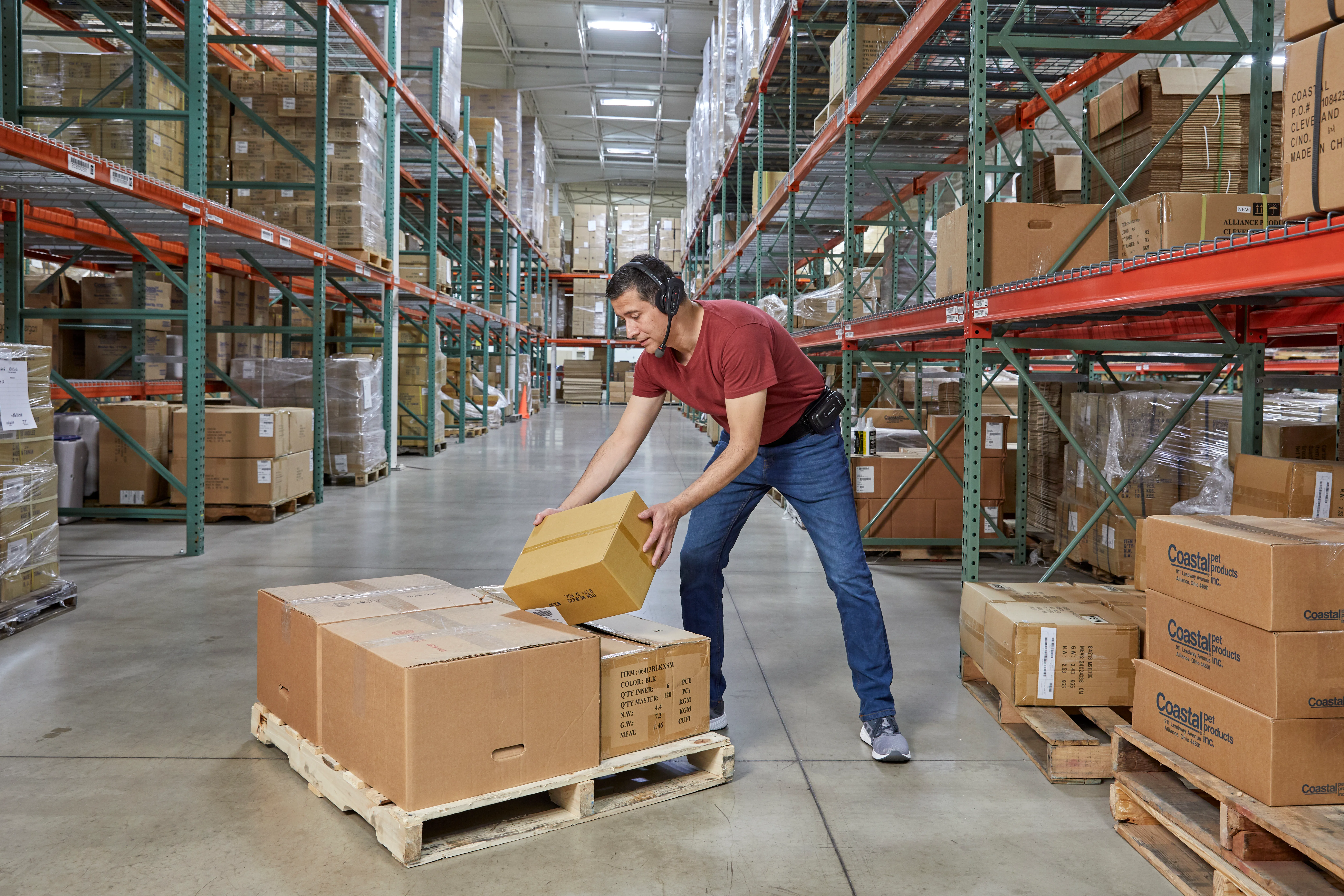 A warehouse operator equipped with a headset and a talkman device, is placing the items on a pallet.